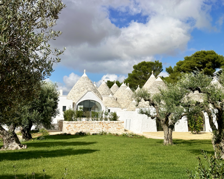 Apulian trulli surrounded by olive trees and cloudy sky.